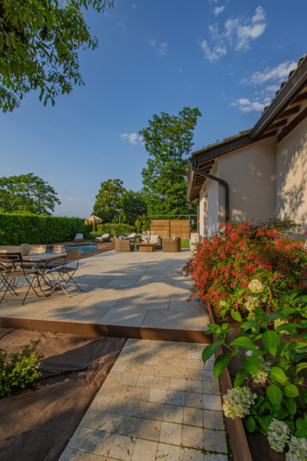 Vaste terrasse aménagée avec des dalles en pierre calcaire, coin repas et salon extérieur près de la piscine. Jardin fleuri luxuriant.