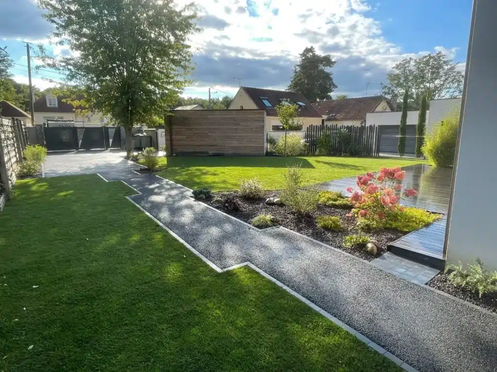 Aménagement paysager moderne avec allée géométrique, pelouse soignée et terrasse en bois dans un jardin ensoleillé.