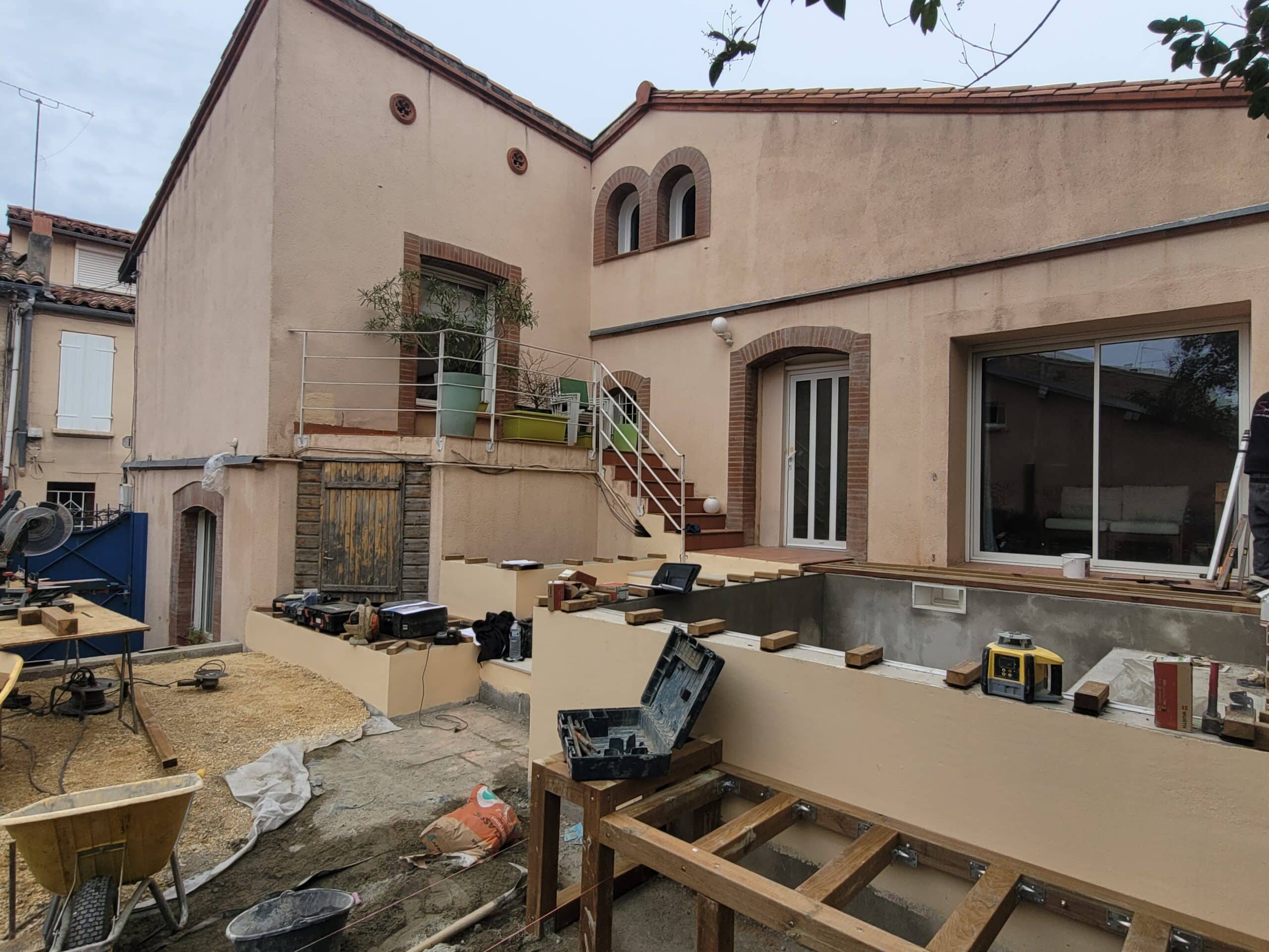 Chantier de construction d'une terrasse bois et piscine dans le jardin d'une maison méditerranéenne avec outils.