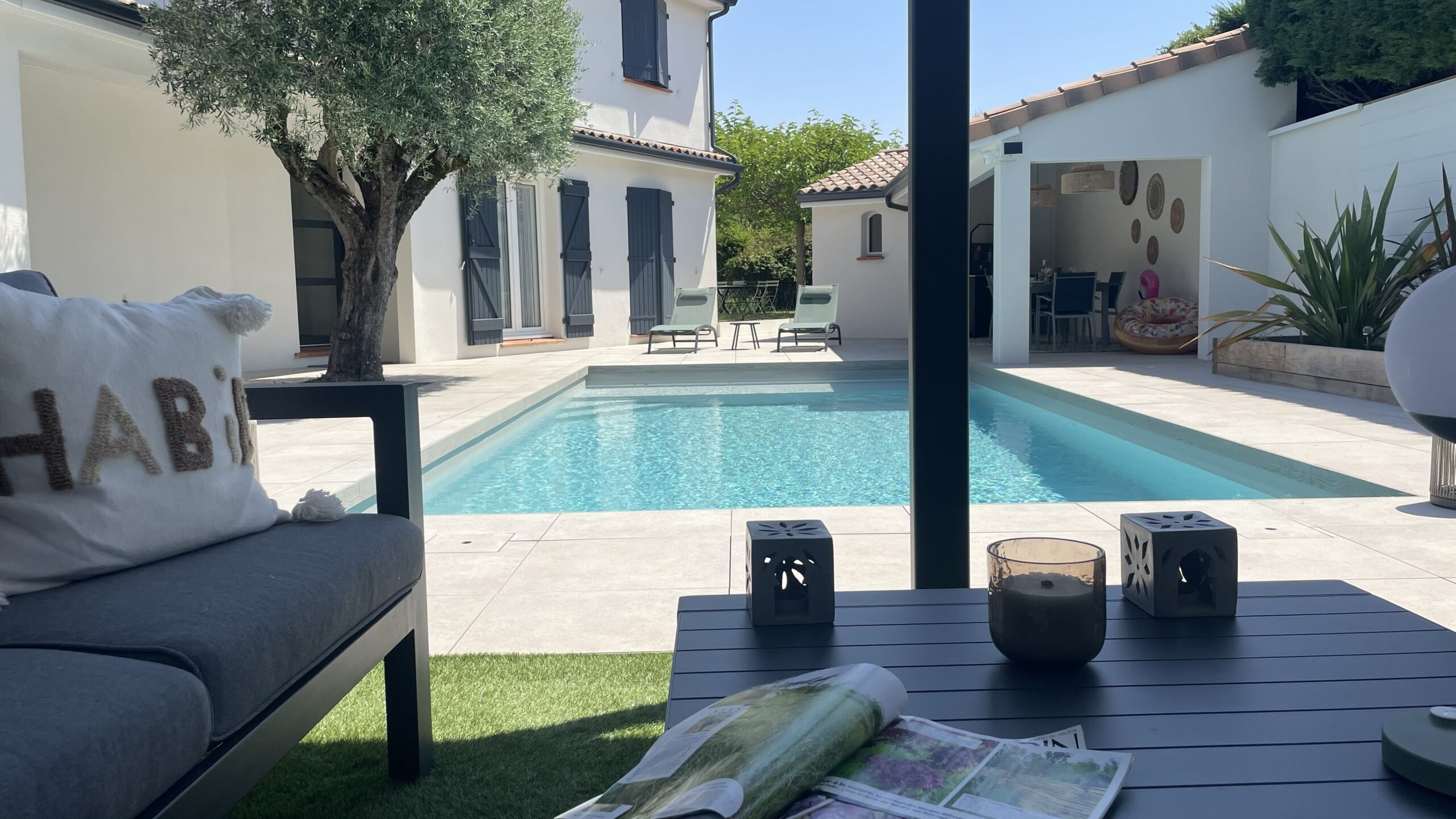 Terrasse avec piscine, maison blanche et mobilier de jardin moderne.